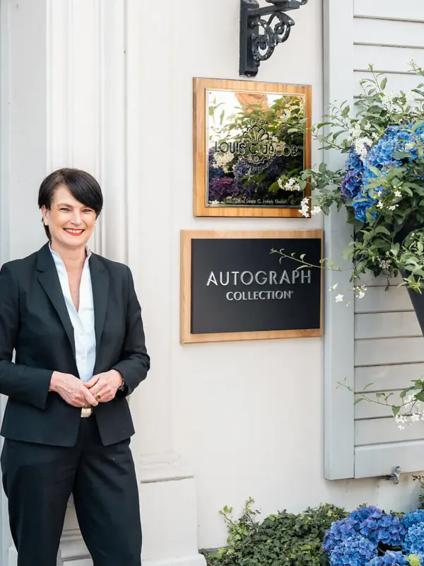 Hoteldirektorin Eingang Die Hoteldirektorin Judith Fuchs-Eckhoff steht vor dem Hoteleingang des Louis C. Jacobs und lächelt..