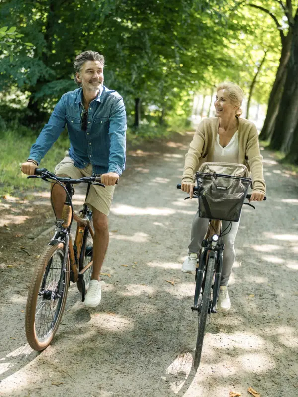 Ein Mann und eine Frau fahren Fahrrad auf einem Fahrradweg gesäumt von Bäumen und Hecken entlang der Elbe.