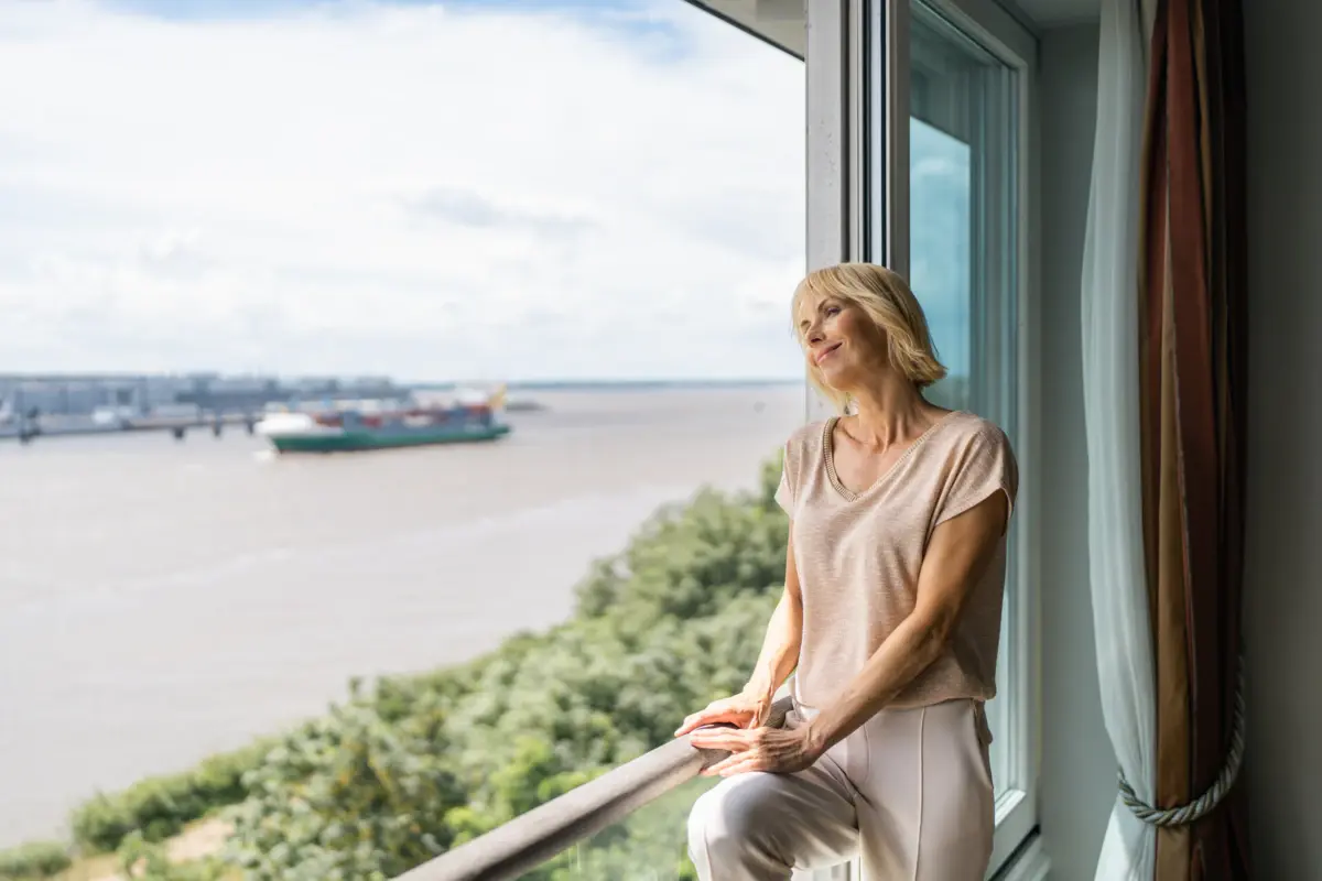 Aussicht Zimmer Eine blonde Frau schaut aus einem großen Fenster in einer Suite des Hotels Louis C. Jacob auf die Elbe und die fahrenden Schiffe.