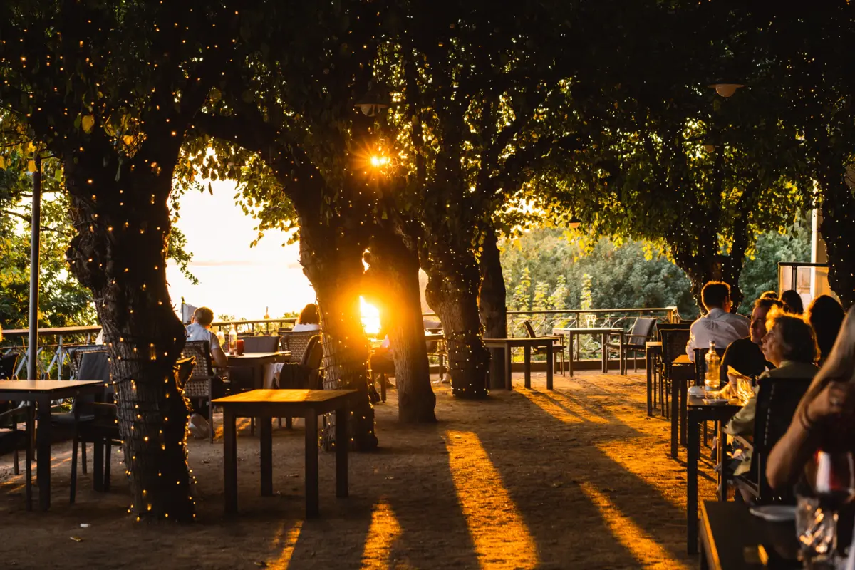Gäste sitzen bei Sonnenuntergang auf der mit Lichterketten beleuchteten Lindenterrasse des Hotels Louis C. Jacob.