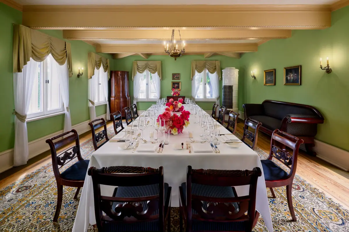 Biedermeier Salon Ein festlicher Veranstaltungsraum mit einer langen Tafel, dunklen Stühlen und roten Blumen auf den Tischen.