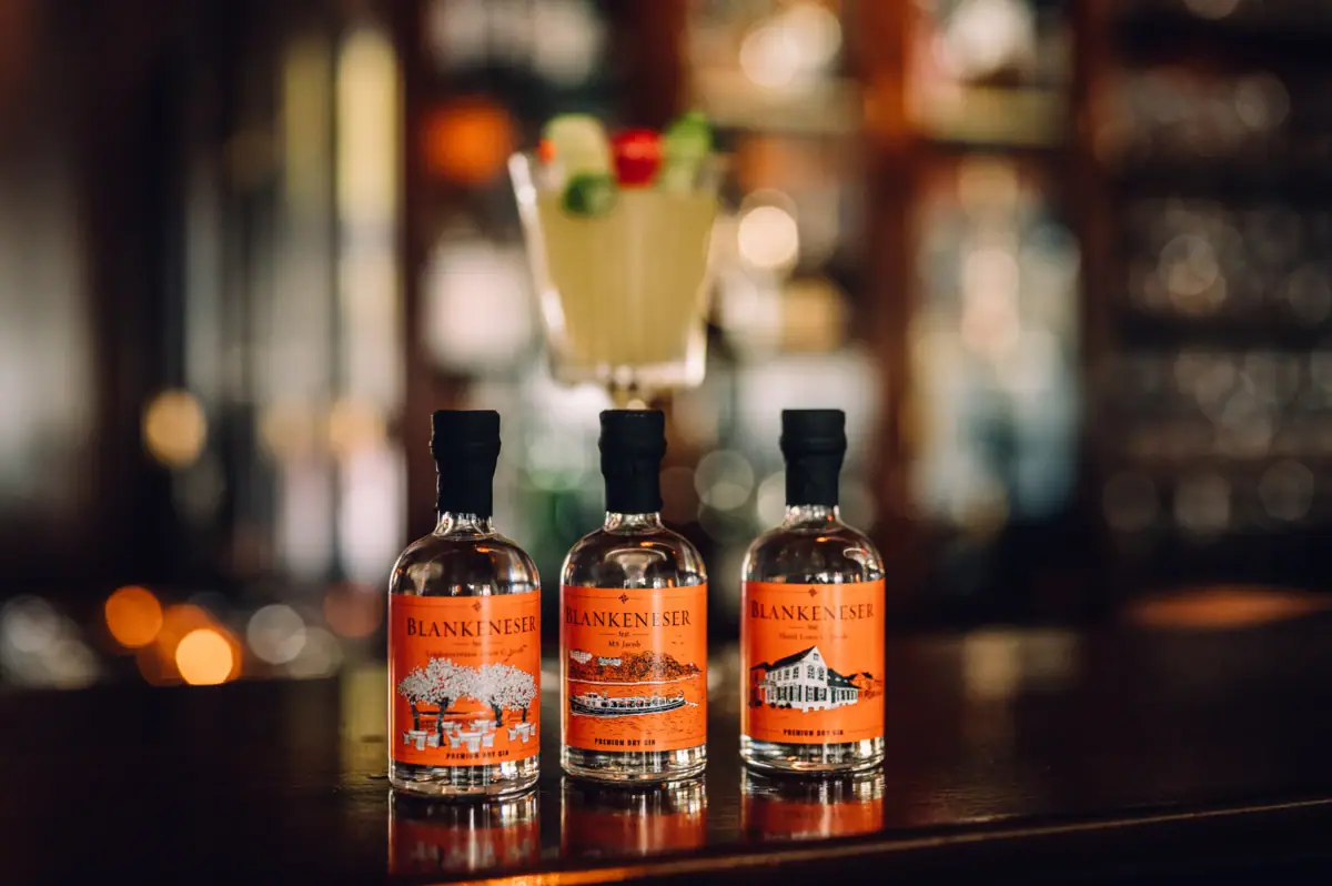Gin Flaschen Drei Flaschen des Blankeneser Premium Dry Gin Collectors Edition "Hotel Louis C. Jacob" stehen auf einem hölzernen Bartresen.