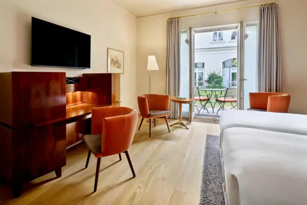 Deluxe Doppelzimmer Louis C. Jacob Hamburg Hotelzimmer mit einem Schreibtisch, einem Bett und einer Terrasse mit Blick ins Grüne im Hintergrund.