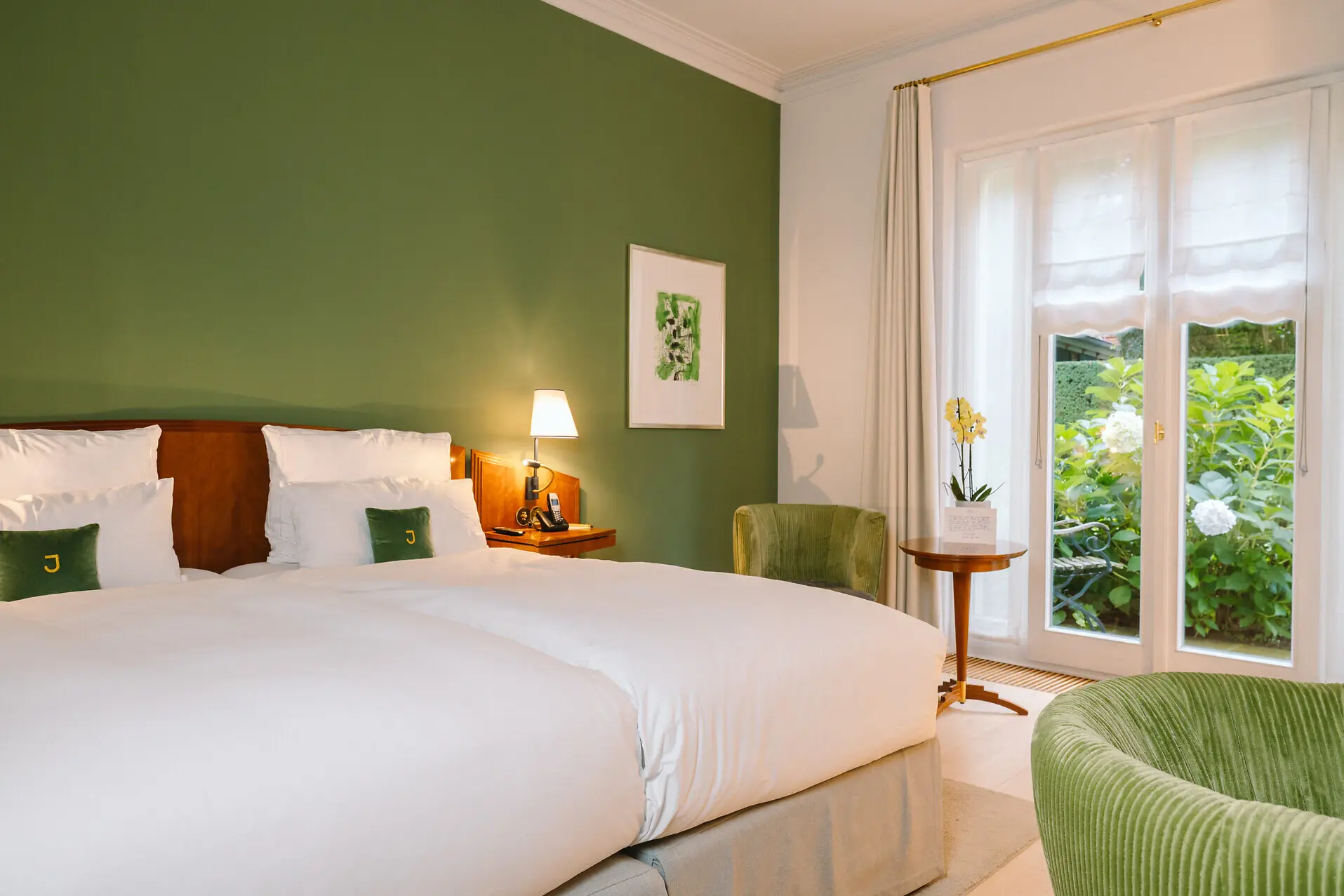 Deluxe Doppelzimmer Louis C. Jacob Hamburg Hotelzimmer mit grünen Wänden, einem Bett und einer Terrasse ins Grüne im Hintergrund.