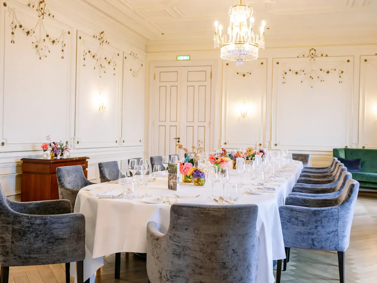 Ein Veranstaltungsraum im Hotel Louis C. Jacob mit einer langen Essenstafel mit blauen gepolsterten Stühlen und eingedecktem Tisch.