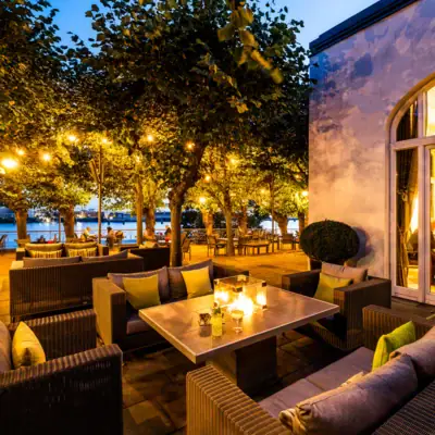 Loungebereich Lindenterrasse Beleuchteter Loungebereich der Lindenterrasse unter freiem Himmel mit Tischen und Sofas.