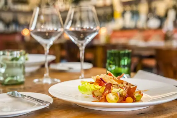 Tellergericht Ein Teller mit Essen auf einem Tisch, umgeben von einem Weinglas und Besteck.