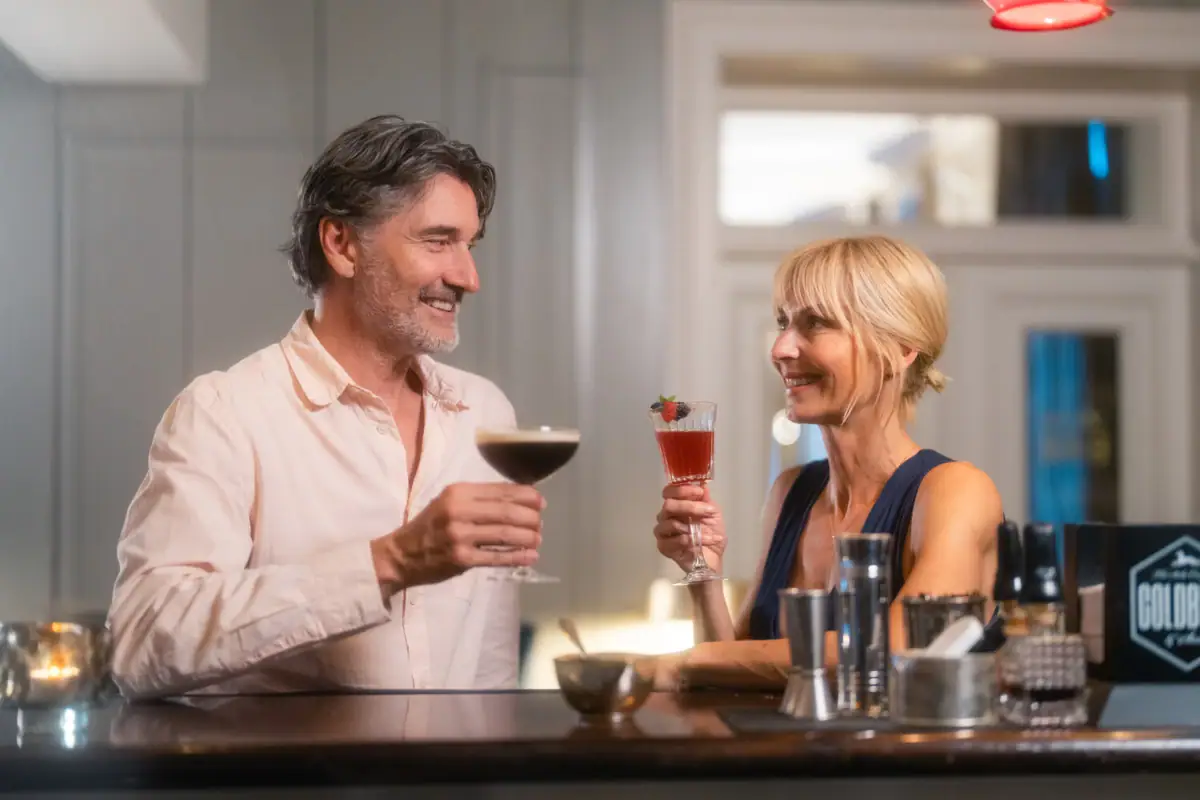 Bar Gäste Eine blonde Frau und ein grauhaariger Mann stehen an der Jacobs Bar und halten je ein Cocktail-Glas in der Hand.