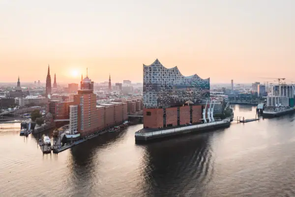 Elbphillharmonie Hamburg Stadtansicht von Hamburg mit der Elbe im Vordergrund und der Elbphillharmonie und der Stadt im Hintergrund bei Sonnenuntergang.
