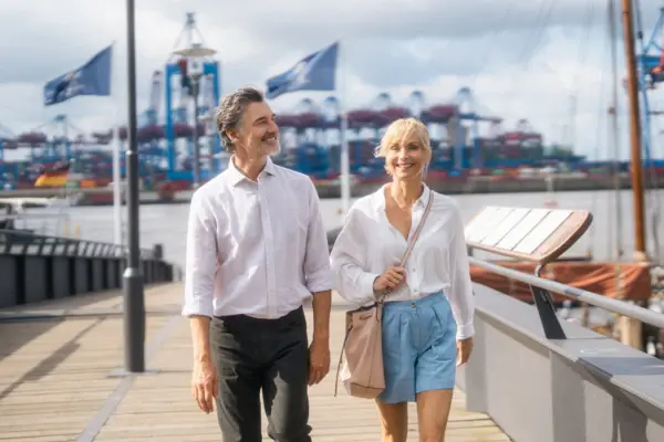 Ein Mann und eine Frau schlendern die Elbpromenade entlang. Im Hintergrund sieht man die Elbe und Schiffe.