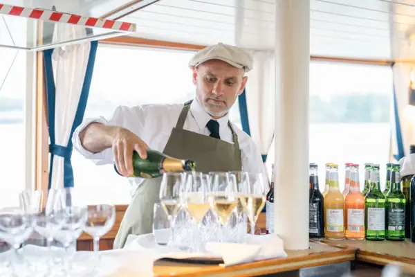 Ein Service-Mitarbeietr gießt Sekt in Gläser auf der MS Jacob.