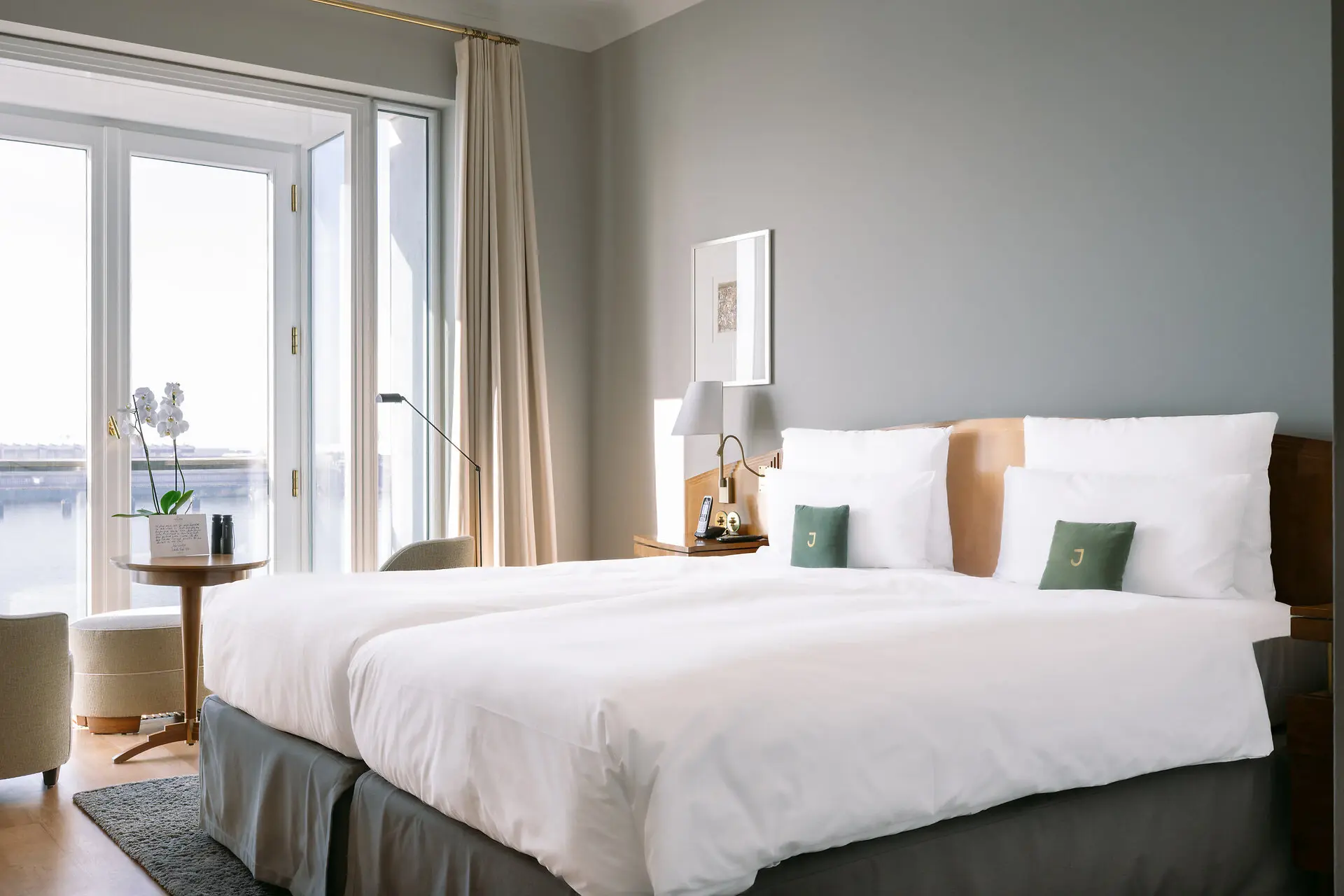 Deluxe Doppelzimmer Elbblick Ein Hotelzimmer mit einem Bett mit weißen Bettlaken und einem großen Fenster mit Blick auf die Elbe.