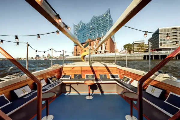 Barkasse MS Jacob Der Außenbereich der Barkasse MS Jacob mit Sitzbänken und Kissen und der Elbphilharmonie im Hintergrund.