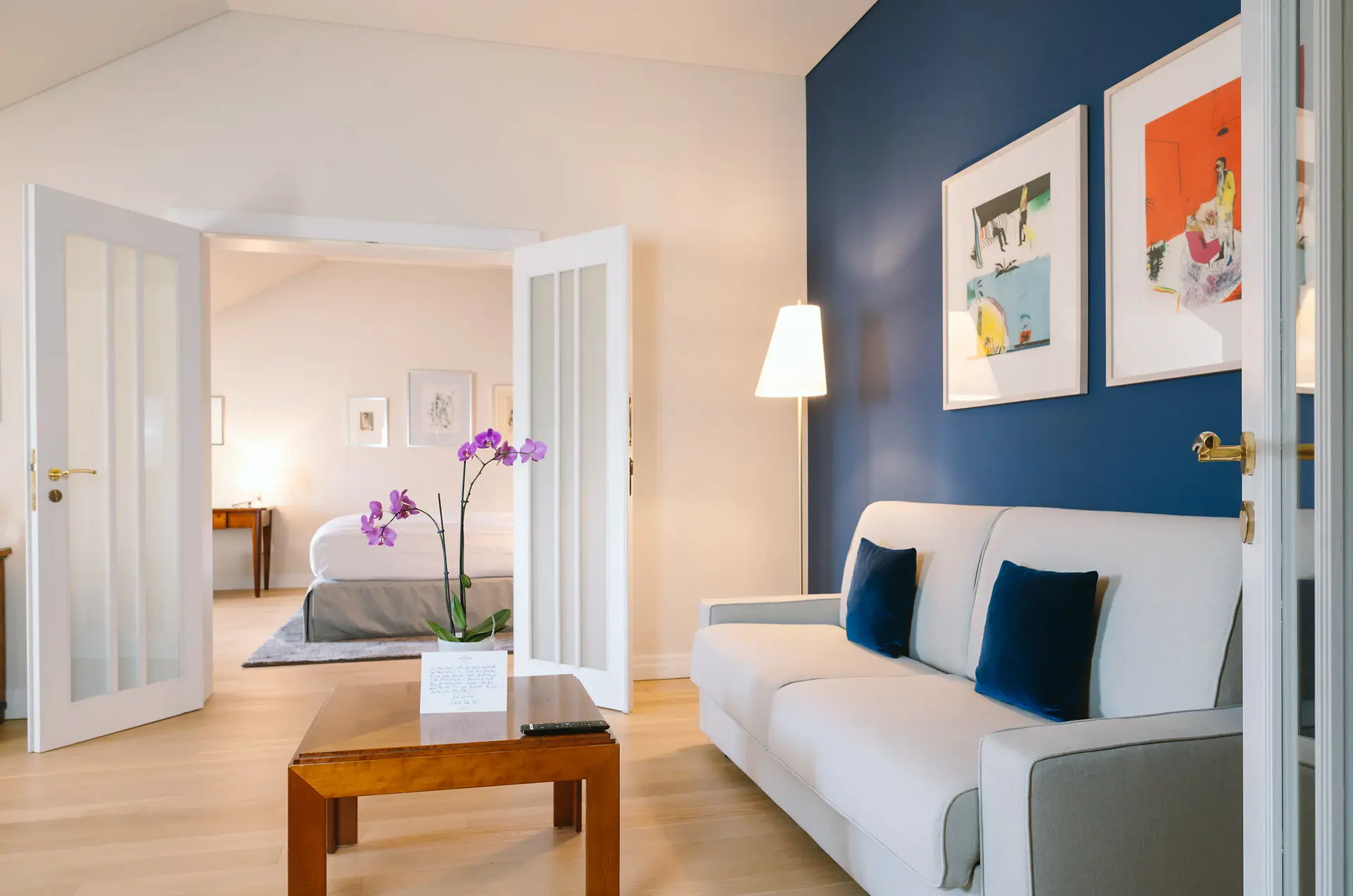 Suite Stadtblick Louis C. Jacob Hotel Ein großes Hotelzimmer mit einem Sofa und einem Tisch im vorderen Raum sowie einem separaten Schlafzimmer im Hintergrund.