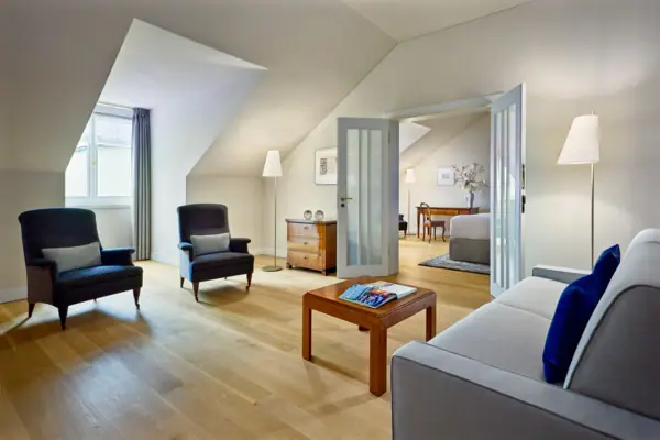 Suite Stadtblick Louis C. Jacob Hotel Ein großes Hotelzimmer mit einem Sofa und einem Tisch im vorderen Raum sowie einem separaten Schlafzimmer im Hintergrund.