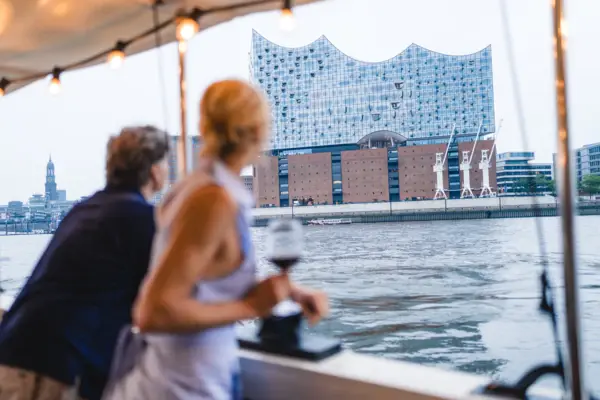 MS Jacob Barkasse Ein Mann und eine Frau stehen an Bord der Barkasse MS Jacob und schauen auf die Elbe und die Elbphilharmonie.