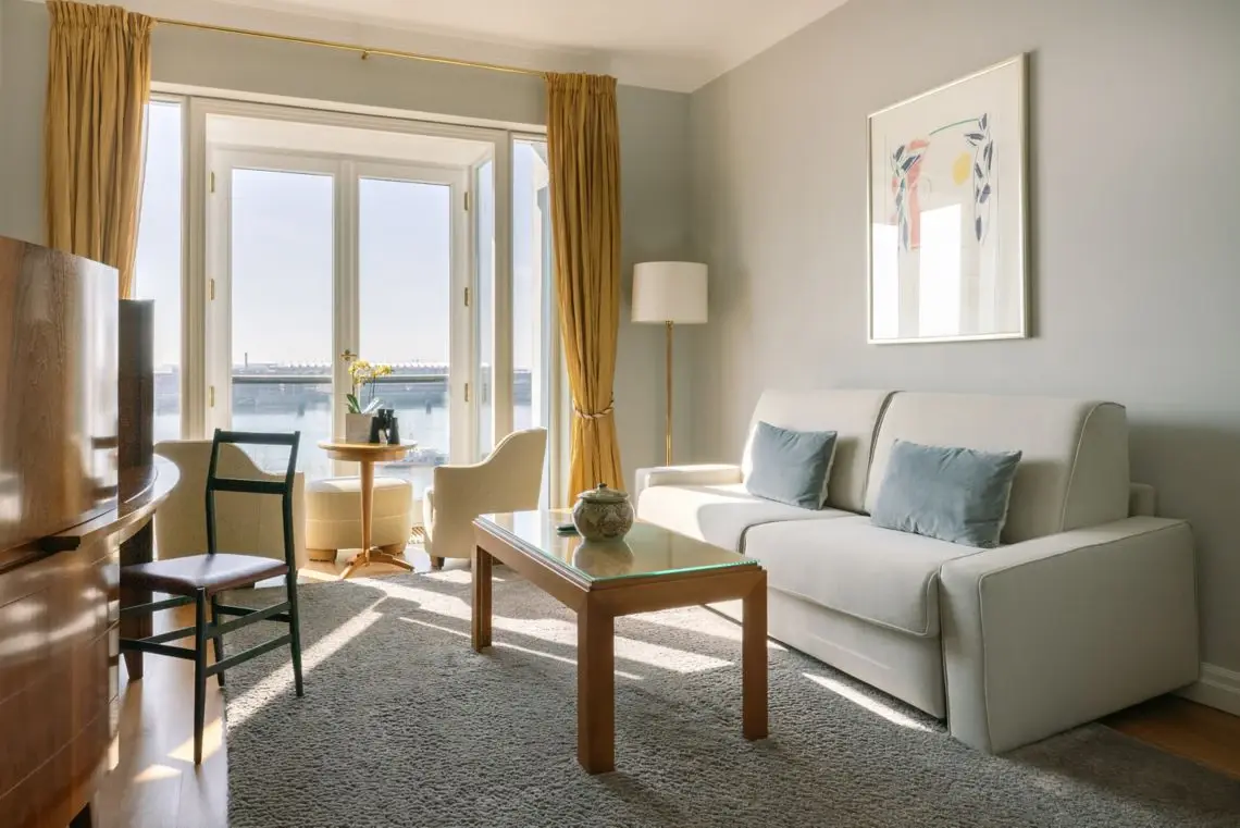 Suite Elbblick Ein gemütlicher Wohnbereich in einem Hotelzimmer mit Couch und Tisch sowie einem Balkon mit Blick auf die Elbe.