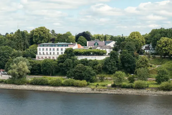 Louis C. Jacob Außenansicht Ein Gebäude in der Nähe eines Gewässers mit Bäumen und Wolken im Hintergrund.