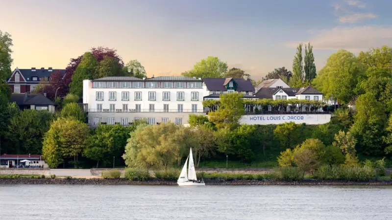 Louis C. Jacob Hotel Hamburg Außenansicht Das Louis C. Jacob Hotel Hamburg von außen mit einem Segelboot davor auf der Elbe.