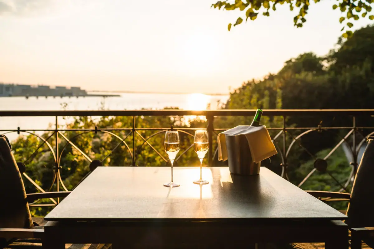 Lindenterrasse Zwei Champagnergläser stehen auf einem Tisch mit Flussblick