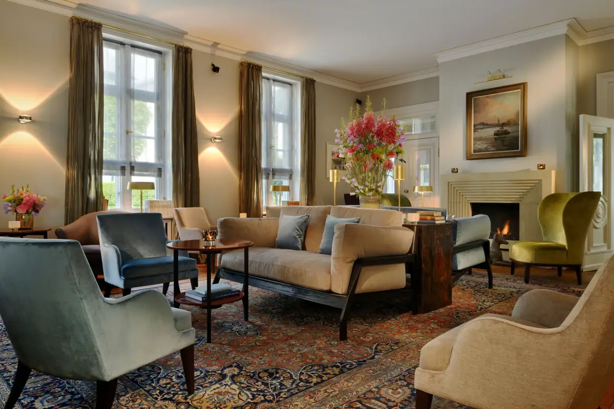 Wohnhalle des Hotels Louis C. Jacob mit Sofas, Sesseln und einem Kamin.