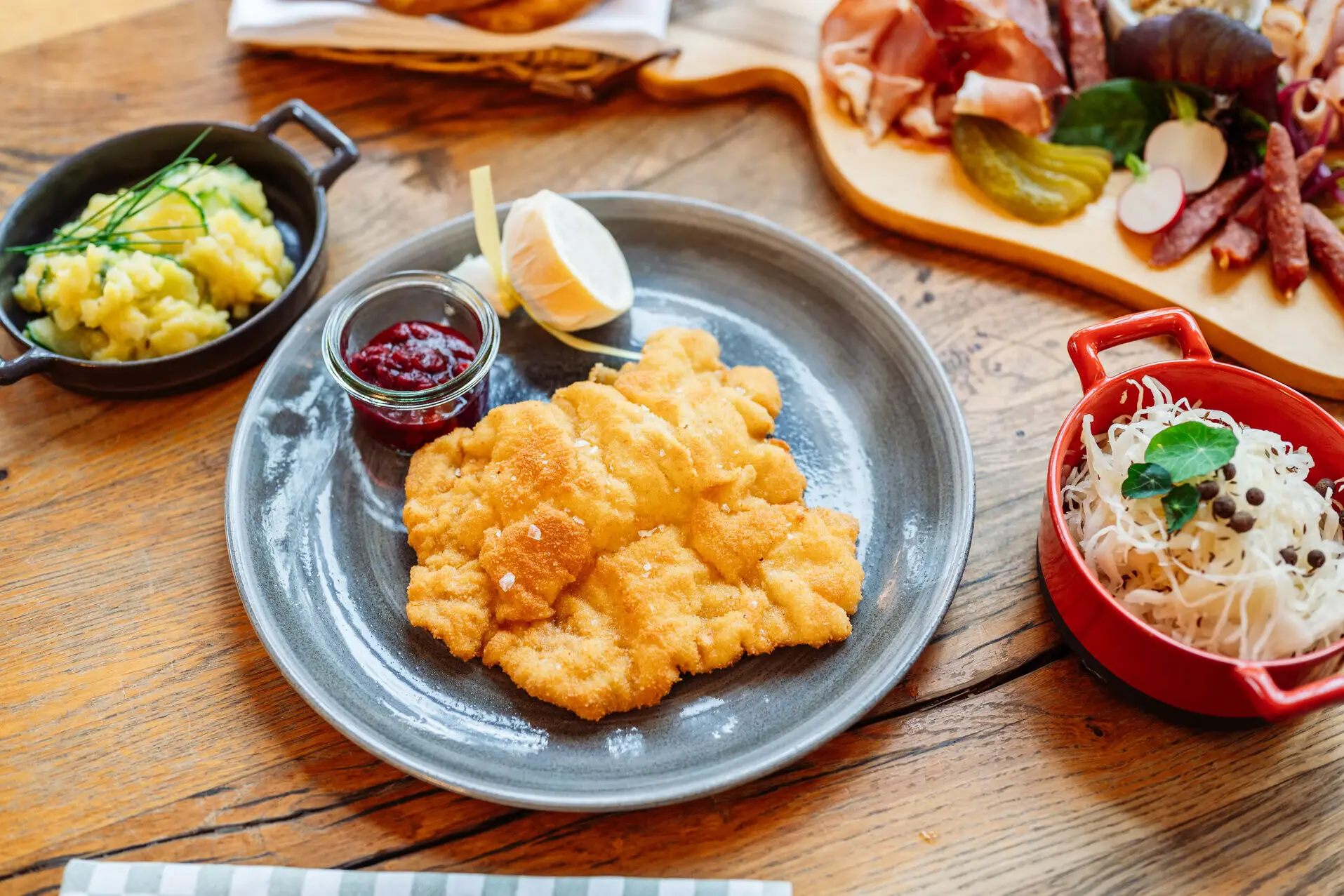 Weinwirtschaft das Kleine Jacob Ein Teller mit einem Schnitzel, Kartoffelsalat sowie eine Wurstplatte auf einem Tisch.